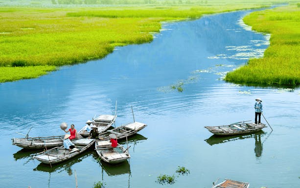 Boats on a river in Tam Coc, Vietnam, with people rowing and lush green landscape.