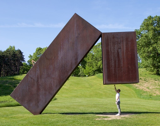 Person interacting with large steel sculpture at Storm King Art Center.