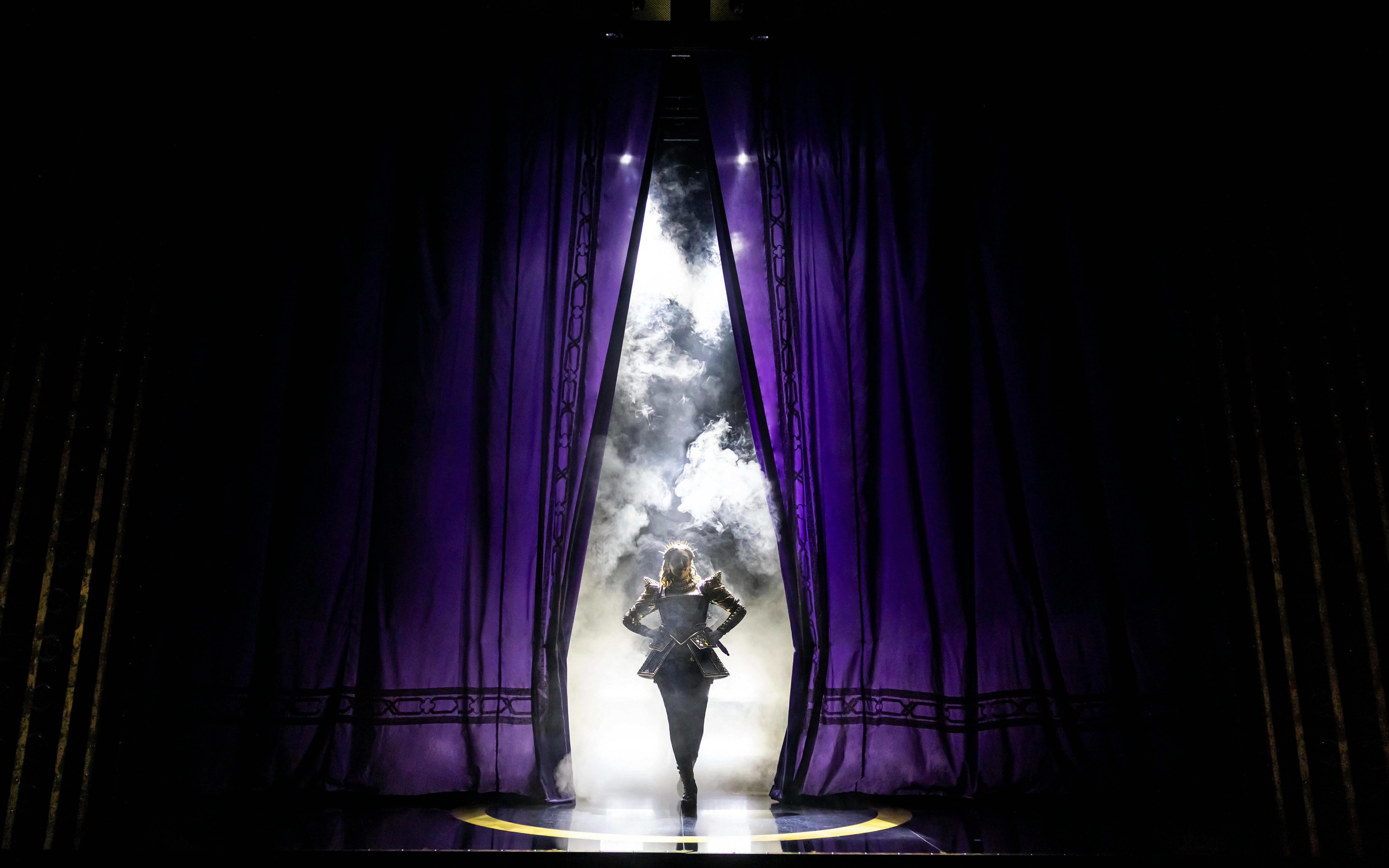 Performer on stage with purple curtains and smoke, Six musical, West End.