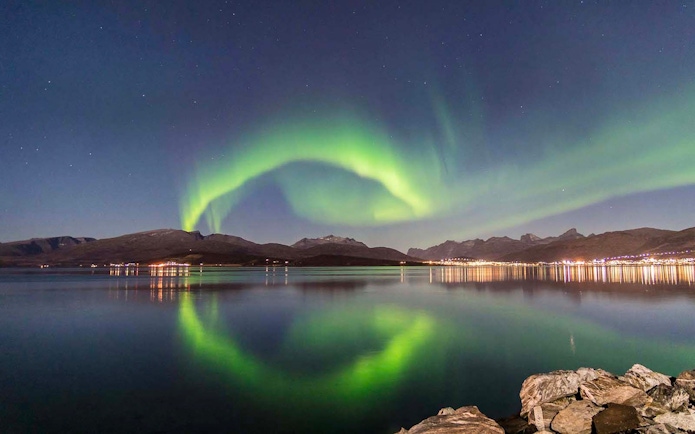 Northern Lights over Tromso fjord with mountain backdrop.