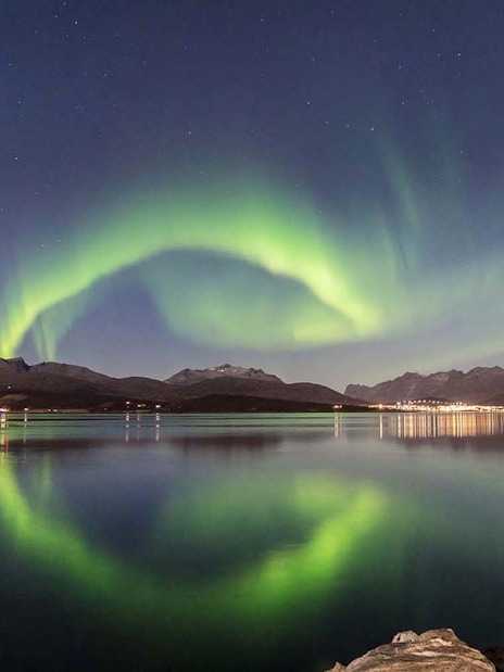 Northern Lights over Tromso fjord with mountain backdrop.