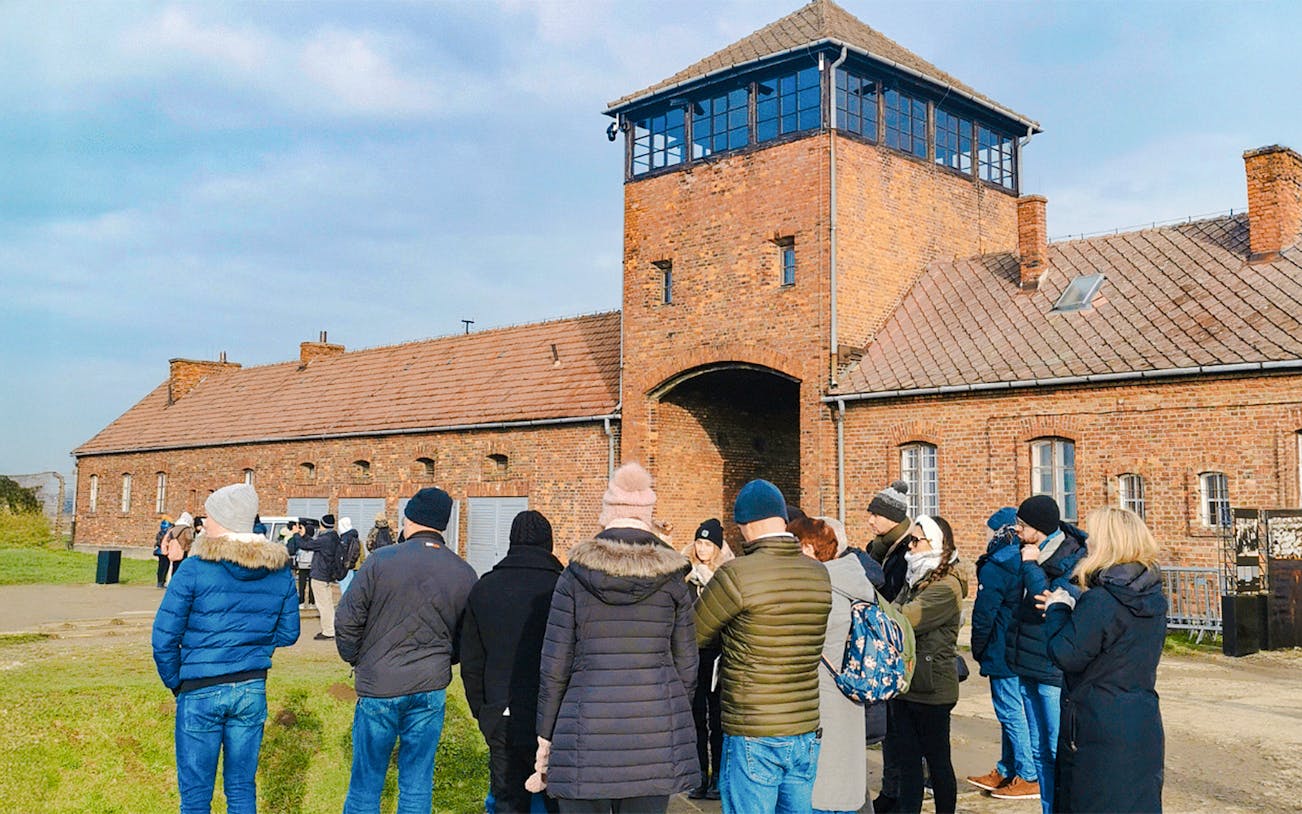Group of tourists at the entrance gate of Auschwitz II during a guided tour.