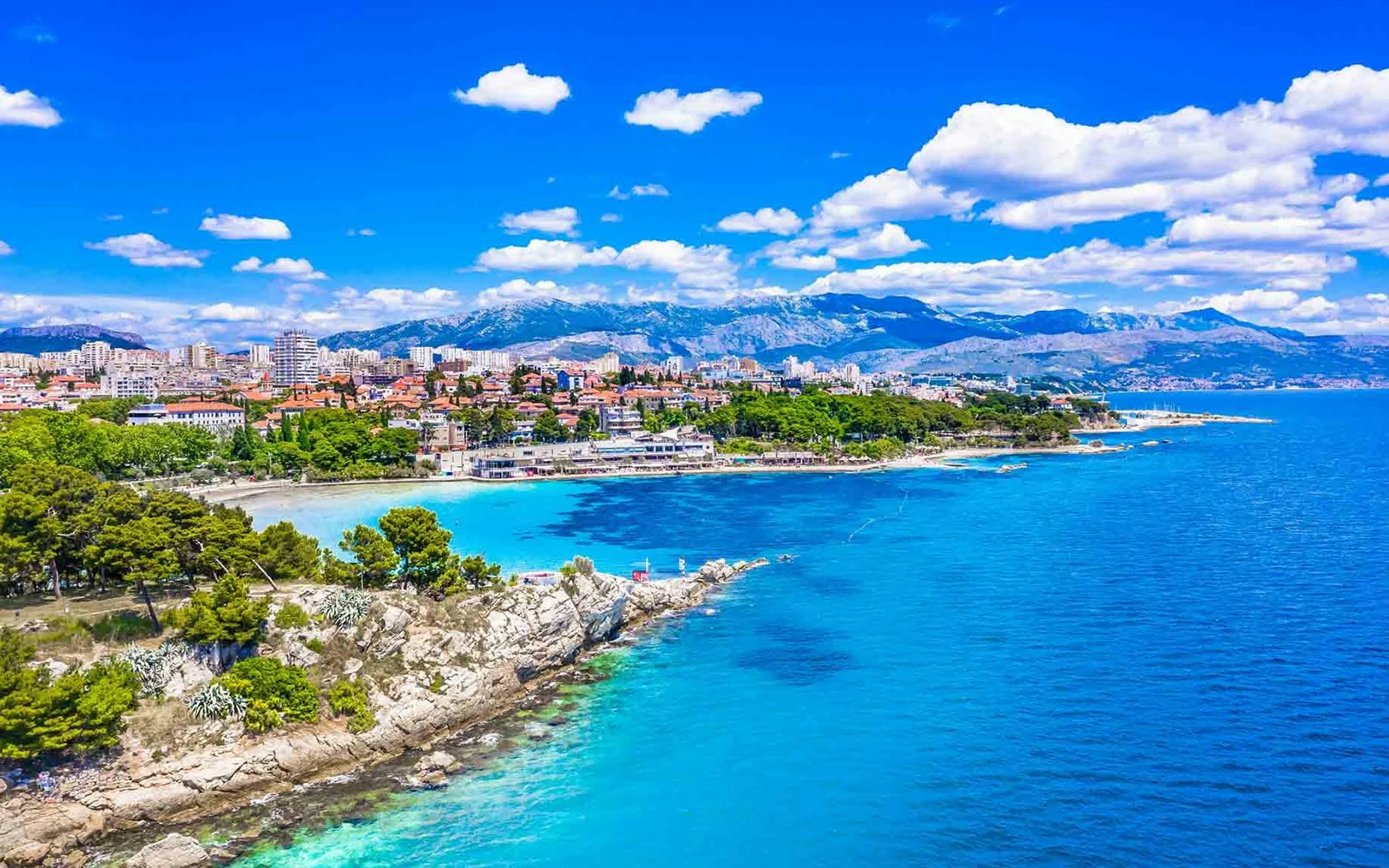 Aerial view of Bačvice Beach in Split, Croatia, with cityscape and mountains in the background.