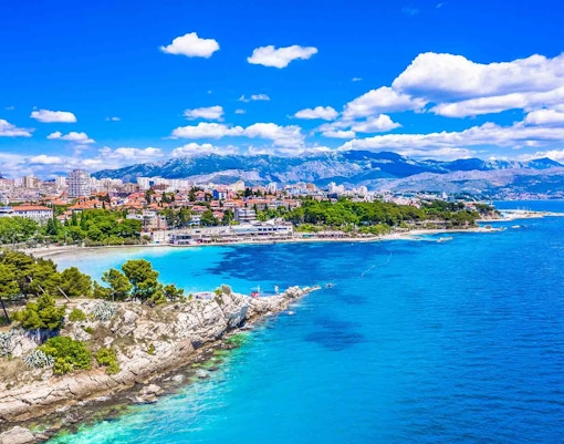 Aerial view of Bačvice Beach in Split, Croatia, with cityscape and mountains in the background.