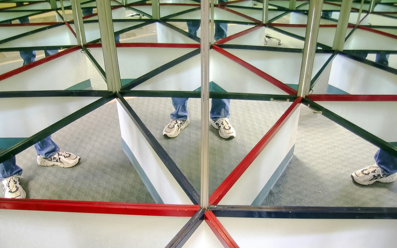 Reflections in a hall of mirrors with geometric patterns and a person's legs.