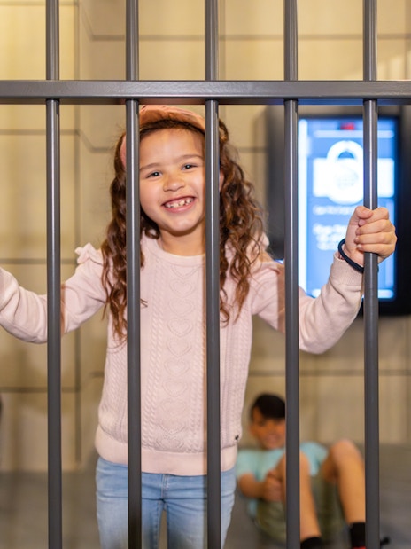 Child smiling behind bars at Monopoly Dreams Melbourne attraction.