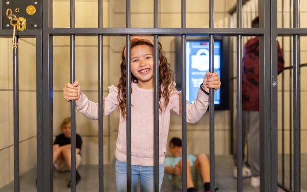 Child smiling behind bars at Monopoly Dreams Melbourne attraction.