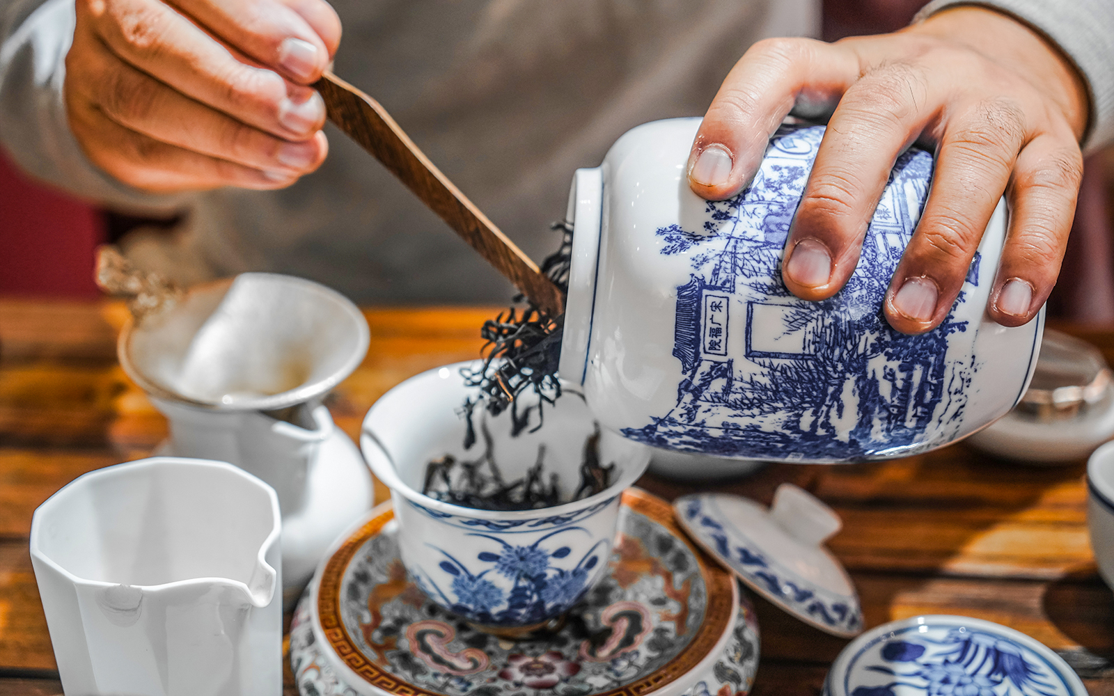 Pouring loose leaf tea into a traditional Chinese teacup with blue patterns.