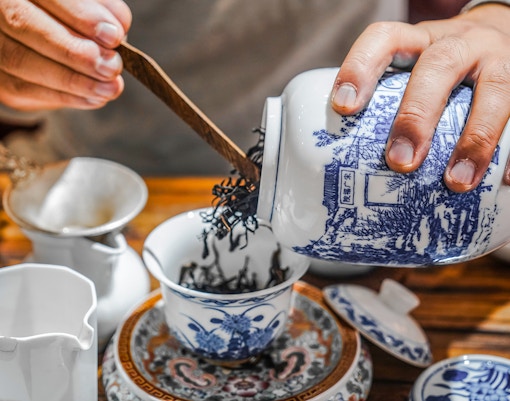 Pouring loose leaf tea into a traditional Chinese teacup with blue patterns.