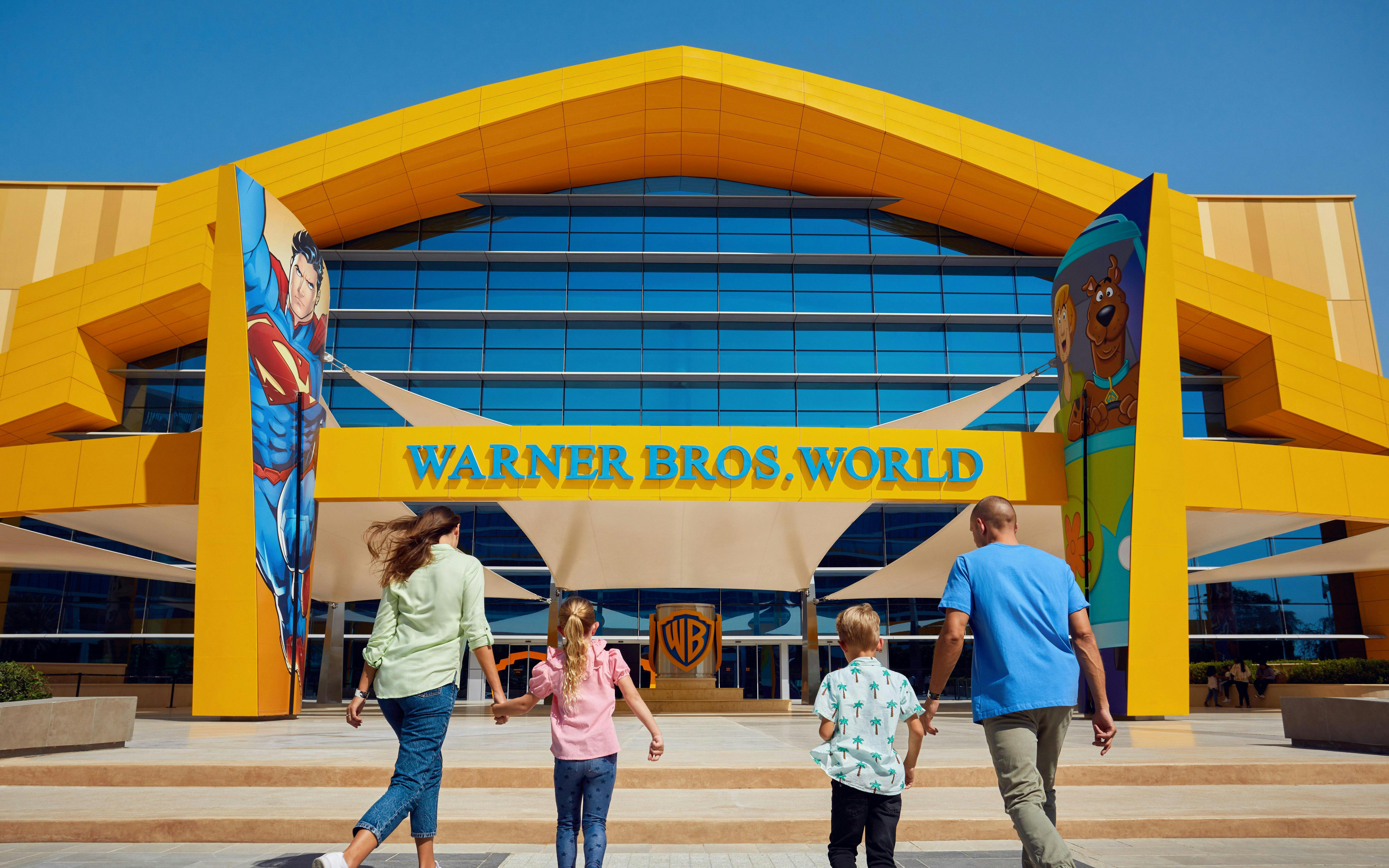 Family entering Warner Bros. World Abu Dhabi with Superman and Scooby-Doo murals.