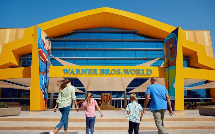 Family entering Warner Bros. World Abu Dhabi with Superman and Scooby-Doo murals.