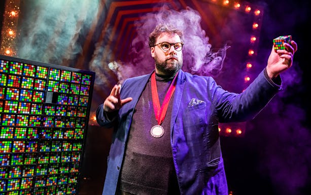 Magician performing with Rubik's cubes on stage, Mind Mangler: Member of the Tragic Circle show.