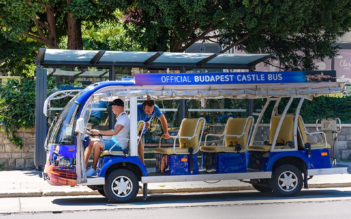 Official Budapest Castle bus parked at a stop with passengers boarding.