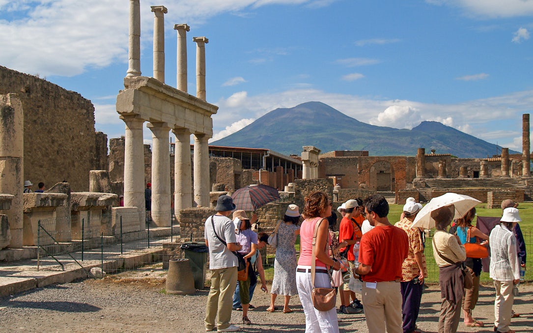 Tourists exploring ancient ruins in Pompeii with Mount Vesuvius in the background.