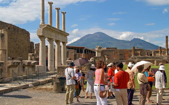 Tourists exploring ancient ruins in Pompeii with Mount Vesuvius in the background.