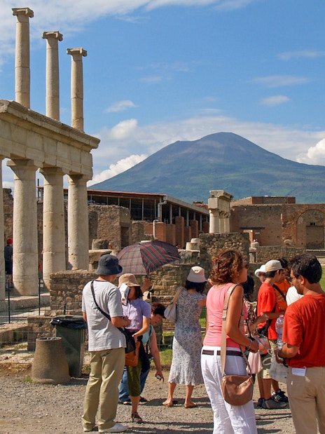 Tourists exploring ancient ruins in Pompeii with Mount Vesuvius in the background.