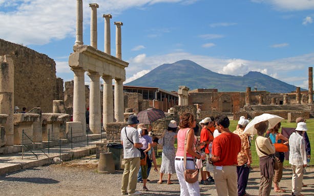 Tourists exploring ancient ruins in Pompeii with Mount Vesuvius in the background.