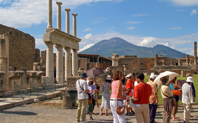 Tourists exploring ancient ruins in Pompeii with Mount Vesuvius in the background.