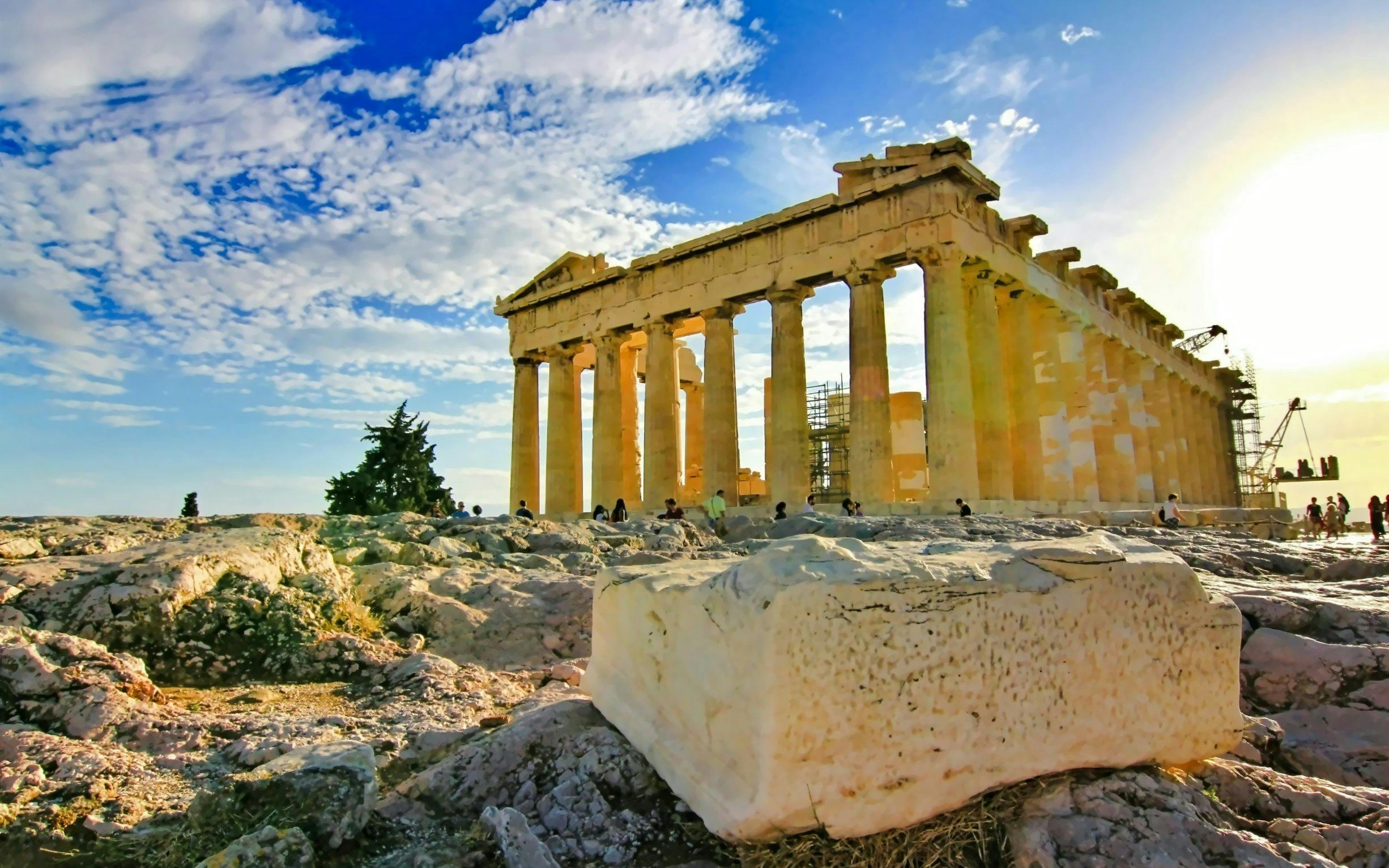 Parthenon temple on Acropolis hill, Athens, with tourists exploring ancient ruins.