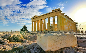 Parthenon temple on Acropolis hill, Athens, with tourists exploring ancient ruins.