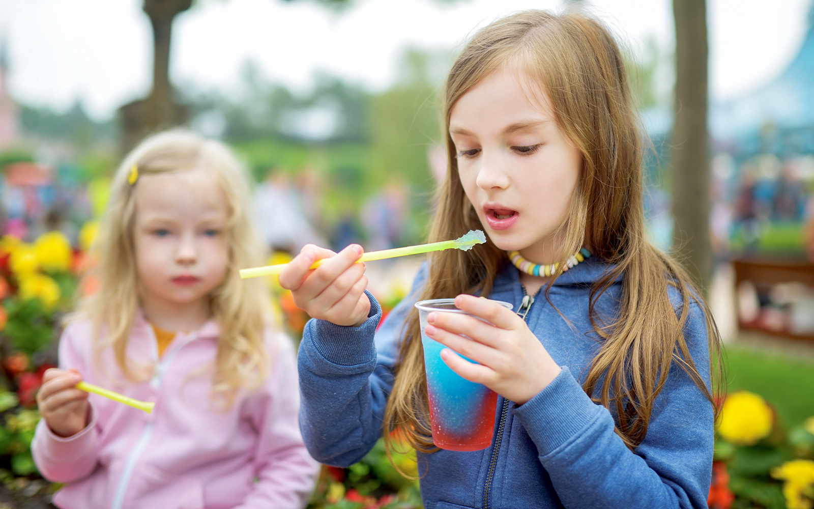 Two sisters enjoying a colorful frozen slushie drink outdoors.