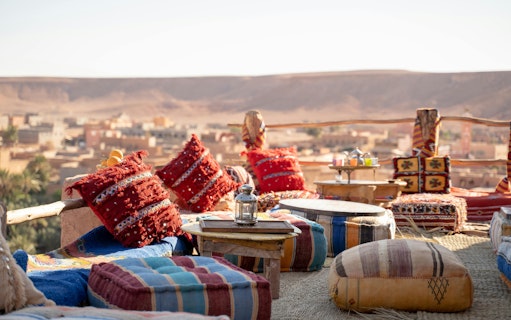 Old lamp on table with colorful cushions at rooftop restaurant overlooking desert town.