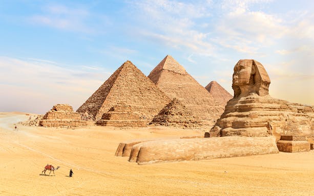 Pyramids of Giza and Sphinx in Egypt with a person leading a camel in the foreground.