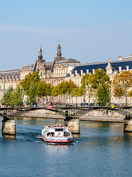 Seine River cruise boat passing under Pont des Arts in Paris.