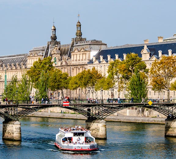 Seine River cruise boat passing under Pont des Arts in Paris.