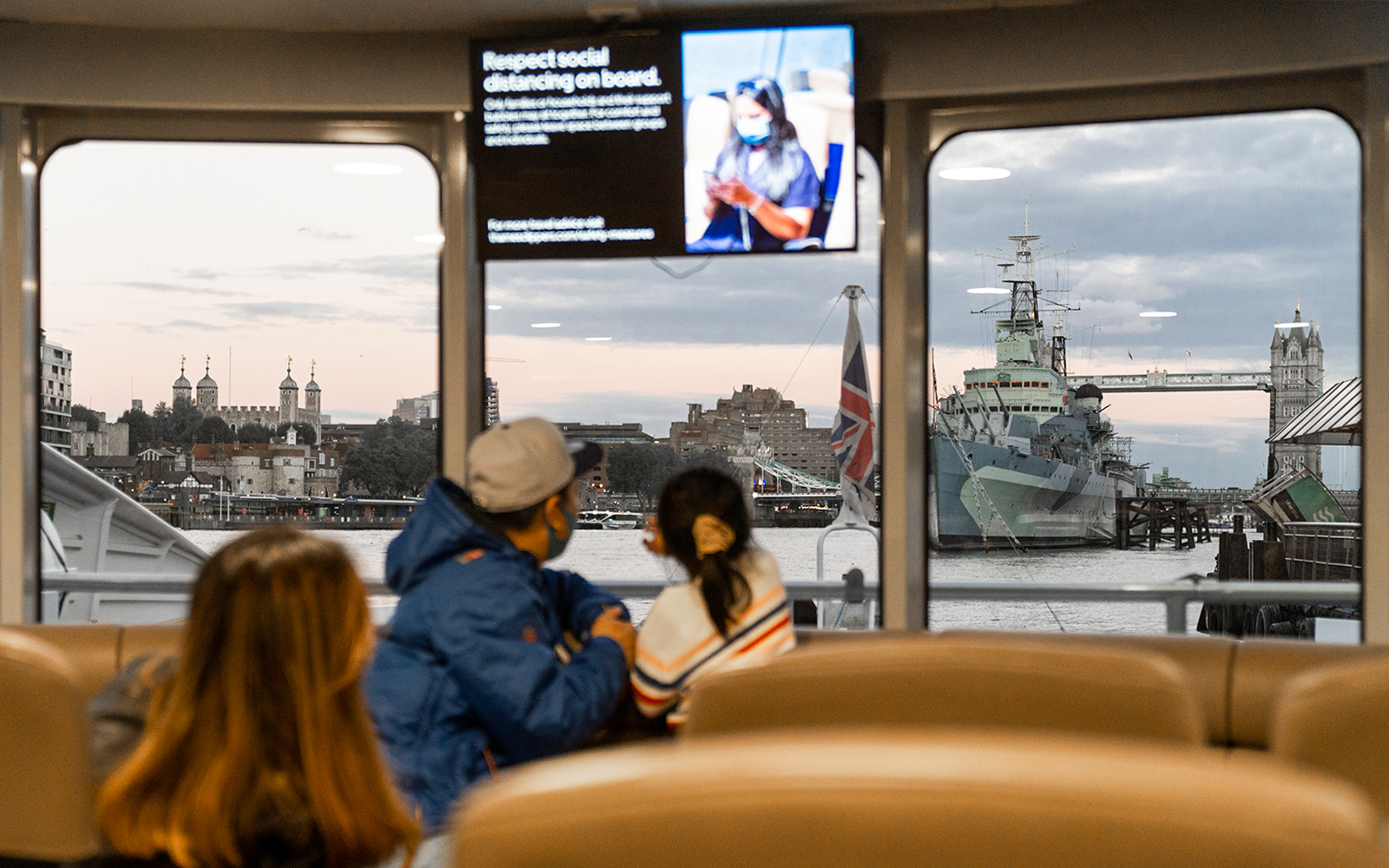 Passengers view Tower Bridge and HMS Belfast from inside the Thames River Uber Boat.