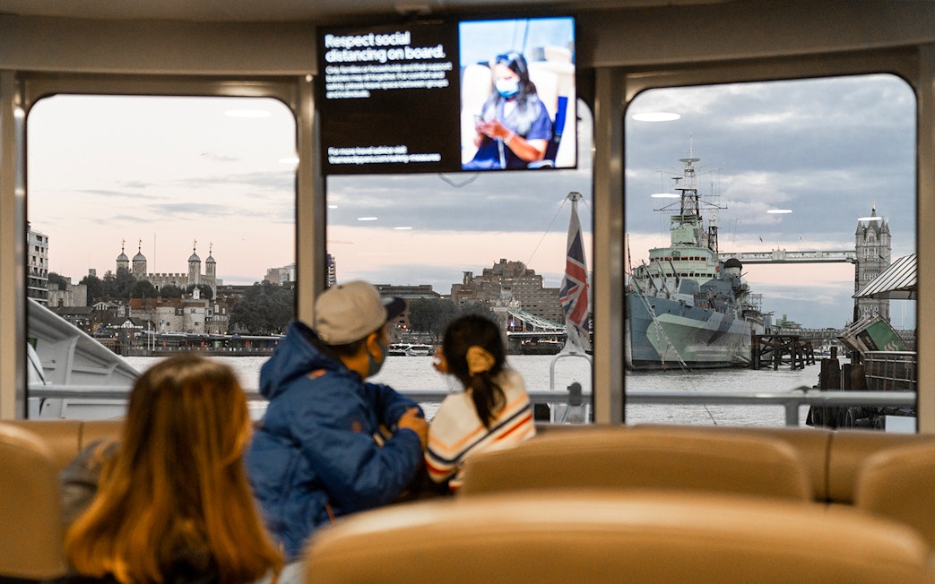 Passengers view Tower Bridge and HMS Belfast from inside the Thames River Uber Boat.
