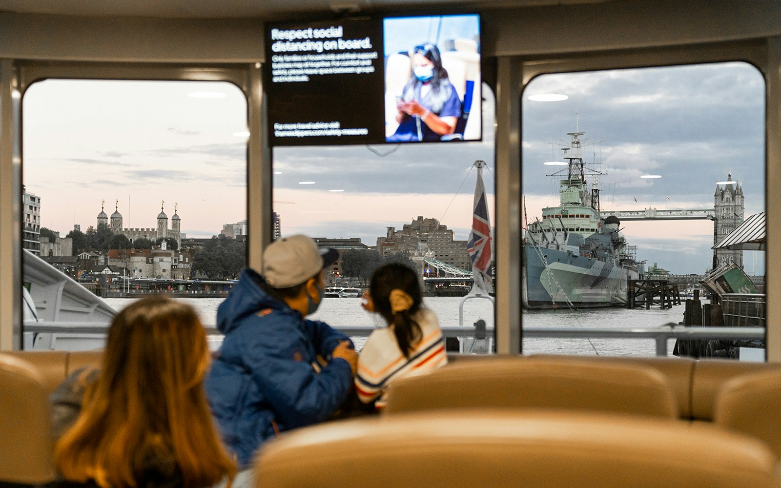 Passengers view Tower Bridge and HMS Belfast from inside the Thames River Uber Boat.