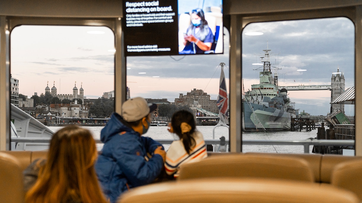 Passengers view Tower Bridge and HMS Belfast from inside the Thames River Uber Boat.
