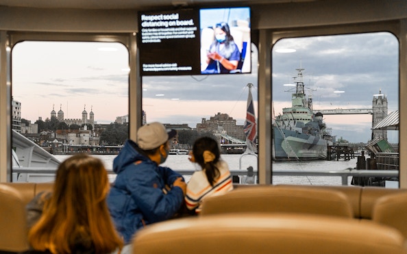 Passengers view Tower Bridge and HMS Belfast from inside the Thames River Uber Boat.