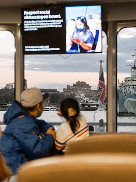 Passengers view Tower Bridge and HMS Belfast from inside the Thames River Uber Boat.