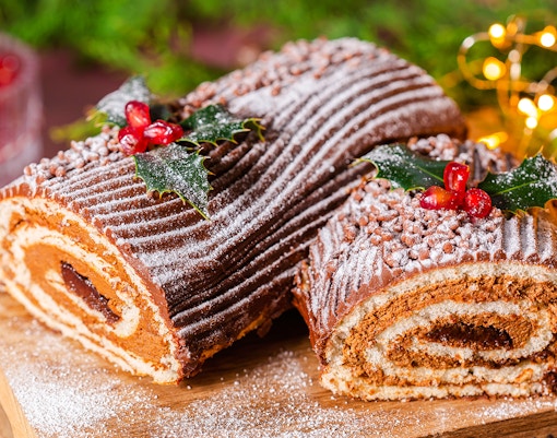 Christmas log cake with chocolate frosting, dusted with powdered sugar and decorated with holly.