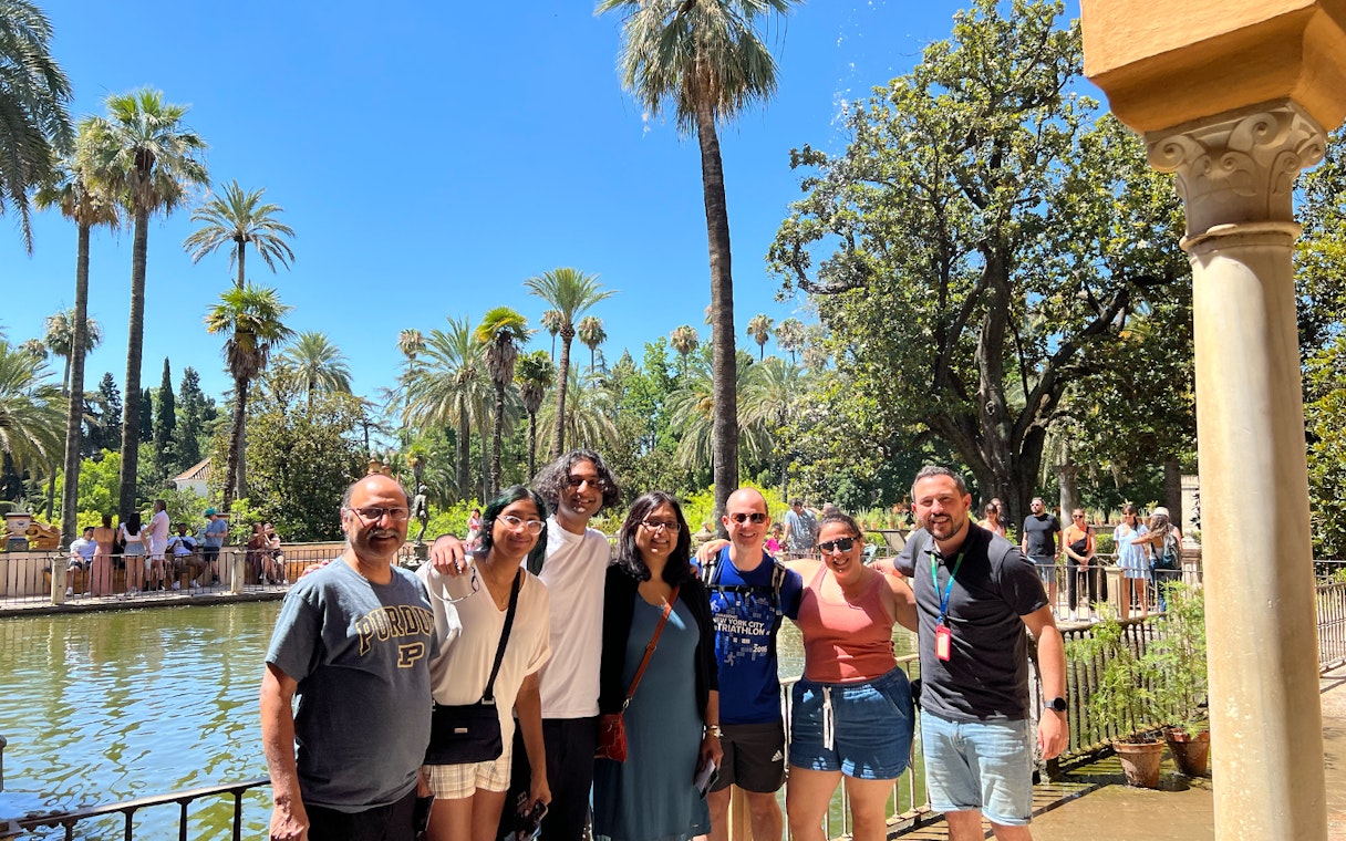 Group of tourists at the Alcázar gardens in Seville, Spain, with palm trees and a pond.