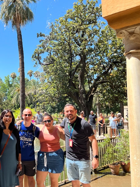 Group of tourists at the Alcázar gardens in Seville, Spain, with palm trees and a pond.