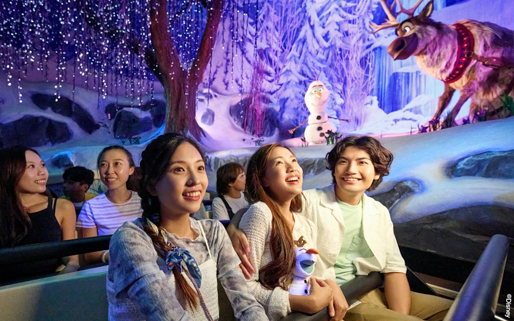 Visitors enjoying Frozen-themed ride at Disneyland Paris with Olaf and Sven in snowy setting.