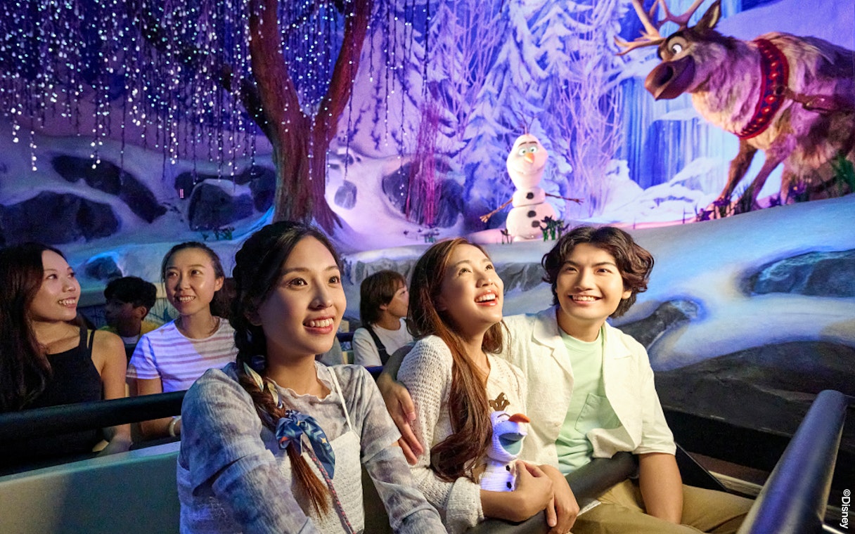 Visitors enjoying Frozen-themed ride at Disneyland Paris with Olaf and Sven in snowy setting.