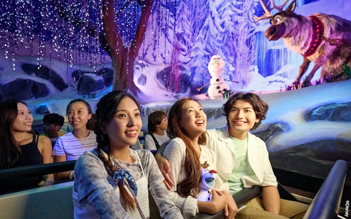 Visitors enjoying Frozen-themed ride at Disneyland Paris with Olaf and Sven in snowy setting.