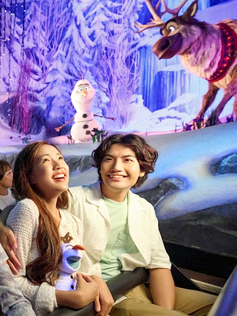 Visitors enjoying Frozen-themed ride at Disneyland Paris with Olaf and Sven in snowy setting.