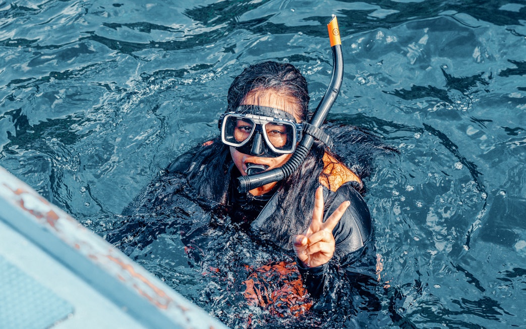 Girl snorkeling underwater in clear blue waters, giving peace sign, Great Barrier Reef, Australia.
