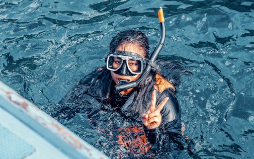 Girl snorkeling underwater in clear blue waters, giving peace sign, Great Barrier Reef, Australia.