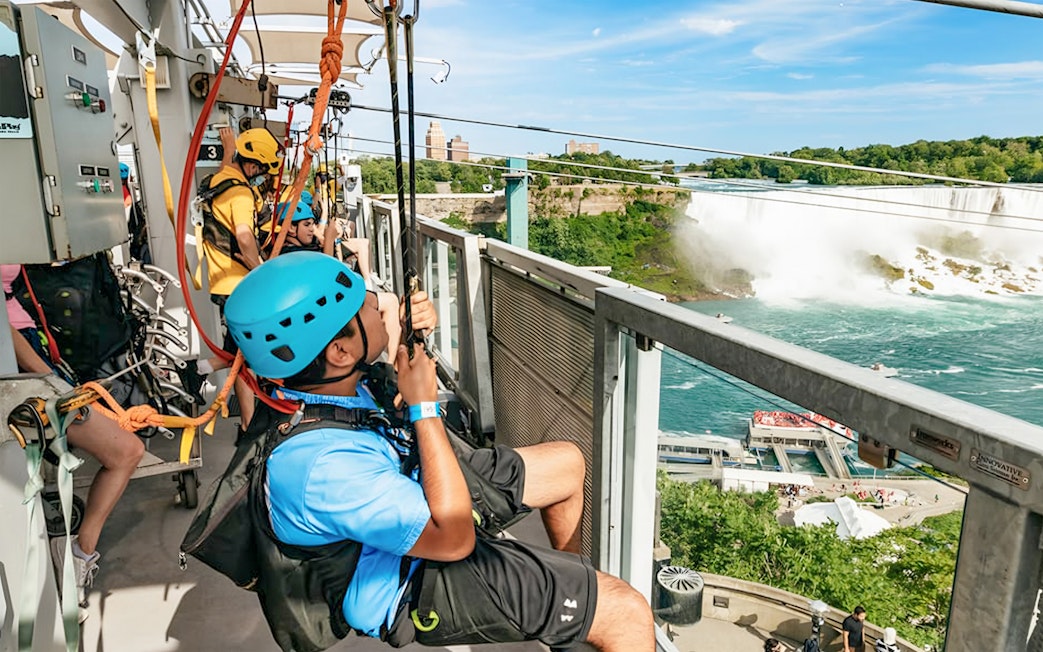 Visitors ziplining towards Niagara Falls with a view of the waterfall and surrounding landscape.