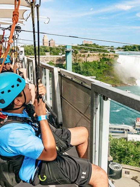 Visitors ziplining towards Niagara Falls with a view of the waterfall and surrounding landscape.