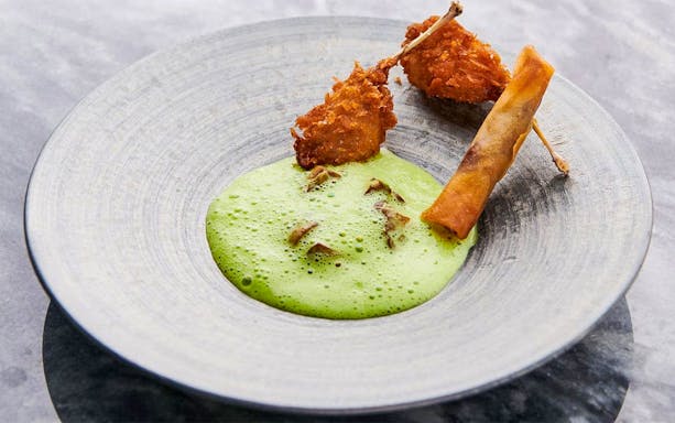 Crispy chicken skewers with green foam sauce on a plate.