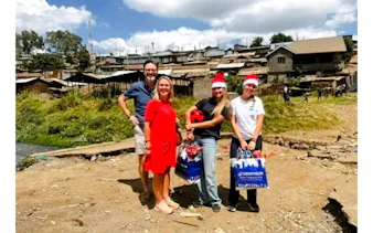 Group of tourists with a local guide in Kibera, Nairobi, holding gifts and wearing Santa hats.