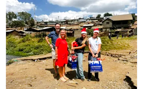 Group of tourists with a local guide in Kibera, Nairobi, holding gifts and wearing Santa hats.