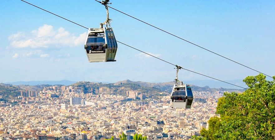 Montjuic Cable Car over Barcelona cityscape with distant hills.